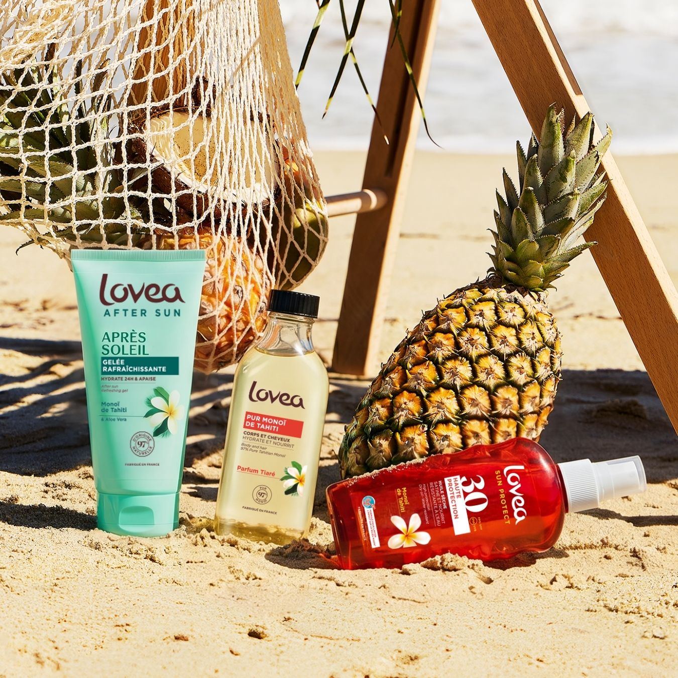 Trois crèmes solaires « Trio Solaire – Protège, Prolonge & Sublime » de Lovea, à base de monoï de Tahiti, sont disposées sur une plage de sable, à côté d’un ananas et d’un sac en filet, tandis que le pied en bois d’une chaise longue se détache sur un arrière-plan baigné de soleil. La scène respire l'ambiance estivale, tandis que les flacons dorés de Lovea, enrichis en Monoï de Tahiti, promettent de protéger, de prolonger et de sublimer votre peau hâlée.