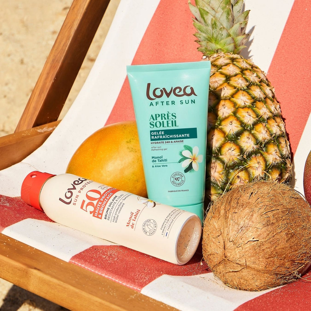 Lovea Duo Solaire Bronzage Doré – Active Protège & Prolonge au monoï de Tahiti, idéal pour des soins solaires haut de gamme et un bronzage doré éclatant, repose sur une chaise longue rayée de rouge et de blanc, à côté d’un ananas, d’une noix de coco et d’une mangue, sur du sable baigné de soleil.