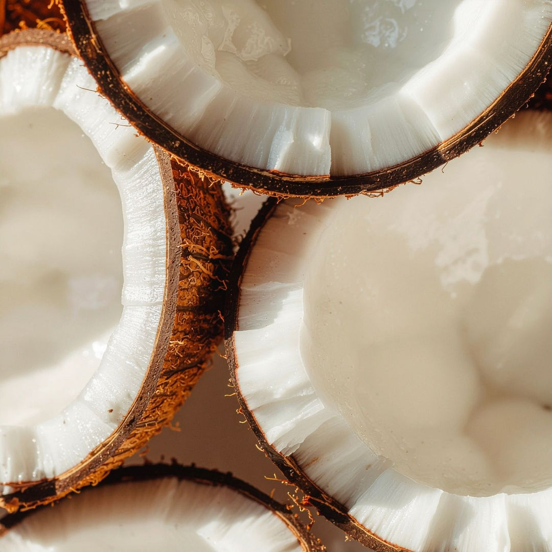 Gros plan sur plusieurs noix de coco coupées en deux, à la chair blanche et à la coque brune et velue, dont certaines sont remplies de crème de coco, disposées les unes contre les autres.